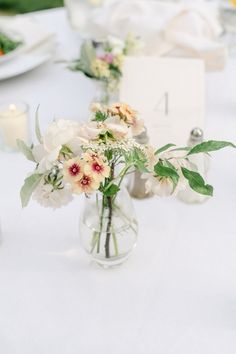 a vase filled with flowers on top of a white table cloth covered dining room table