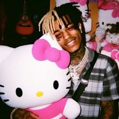 a man with dreadlocks holding a hello kitty stuffed animal in front of his face