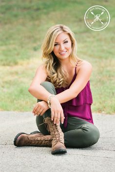 a woman sitting on the ground with her legs crossed, wearing boots and looking at the camera