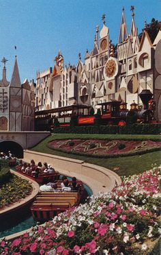 an amusement park with lots of flowers in the foreground and people riding on boats