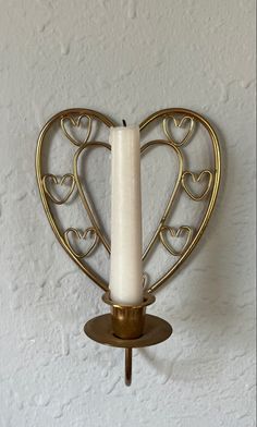 a candle holder with two hearts on it and a lit candle in the middle, against a white wall