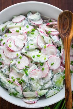 a white bowl filled with cucumber and radishes next to a wooden spoon