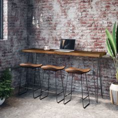 three stools sit in front of a brick wall with a laptop on the desk