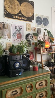 a green dresser topped with lots of potted plants next to a wall covered in pictures