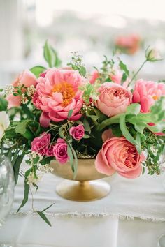 a vase filled with pink flowers sitting on top of a white tablecloth covered table