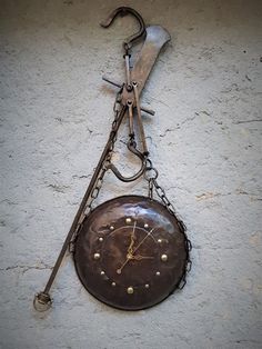 an old clock hanging on the side of a building with chains and tools attached to it