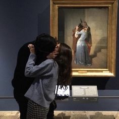 a man and woman are kissing in front of a painting on display at the museum