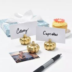 two place cards with gold pumpkins on them and a cupcake in the background