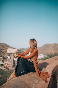 a woman sitting on top of a rock looking at the sky and buildings in the background