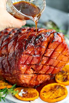 someone is drizzling sauce on top of a roasting ham with orange slices