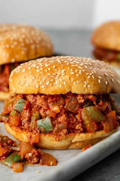 two sloppy joes on a tray with some other food in the backgroud