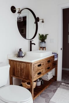 a white toilet sitting next to a wooden vanity in a bathroom under a round mirror