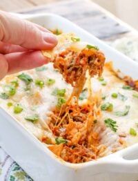 a person dipping some food into a casserole dish with cheese and green onions