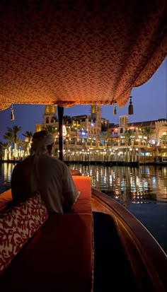 a man is sitting in a boat on the water at night with city lights behind him