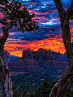 the sun is setting over mountains and trees in the foreground, with red rock formations in the background