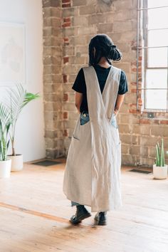 a woman standing in front of a brick wall with an apron over her shoulder and black hair