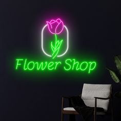 a neon sign that says flower shop in front of a dark room with a chair