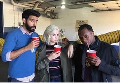 three people standing in a room holding cups with straws and drinking from red cups