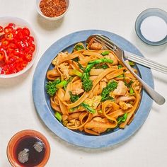 a blue plate topped with pasta and broccoli next to bowls of sauces