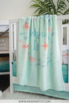 a child's bed with a blue and pink blanket on it, next to a potted plant