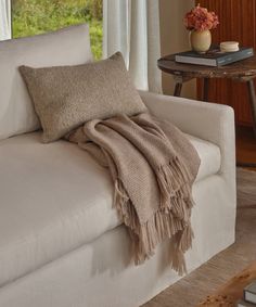 a white couch with a blanket on it next to a table and flowers in a vase