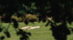 a person laying on the ground in a grassy field with trees and bushes behind them