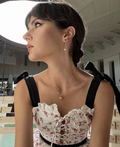 a woman wearing a white and black dress sitting on top of a wooden bench next to a swimming pool