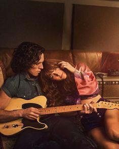 a man sitting next to a woman while holding a guitar in front of her face