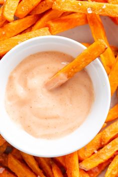 a white bowl filled with dip surrounded by sweet potato fries