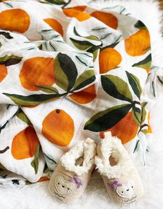 two pairs of baby shoes sitting on top of a white fur covered floor next to an orange print blanket