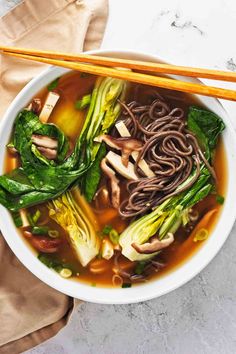 a white bowl filled with noodles and vegetables next to chopsticks on top of a table