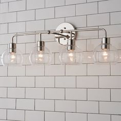 a bathroom light with four bulbs on the wall and white brick walls behind it,