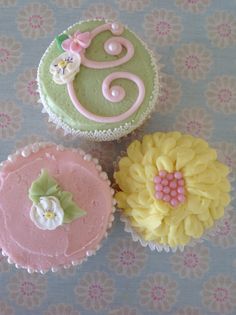 three decorated cupcakes sitting on top of a blue tablecloth with flowers and swirl designs