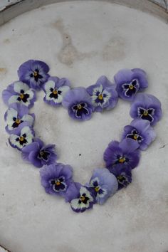 purple and white pansies arranged in the shape of a heart on top of a table