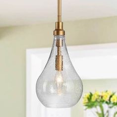 a clear glass light hanging from a ceiling fixture in a room with flowers on the table