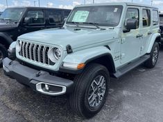 the front end of a light blue jeep parked in a lot next to other vehicles