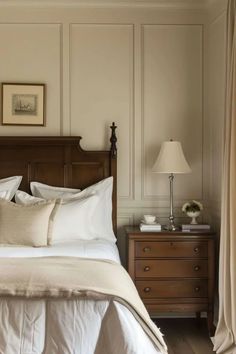 a bed with white linens and pillows in a bedroom next to a dresser, lamp and pictures on the wall