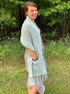 a woman standing in the grass wearing a blue crochet shawl and sandals