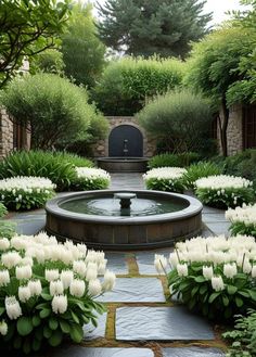 an outdoor fountain surrounded by white flowers and greenery