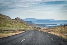 an empty road in the middle of nowhere with mountains in the background