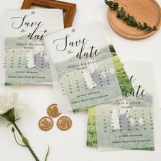 wedding save the date cards and coins on a table with white flowers, greenery and a wooden frame