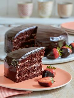 a slice of chocolate cake on a plate with strawberries in the foreground and another piece missing