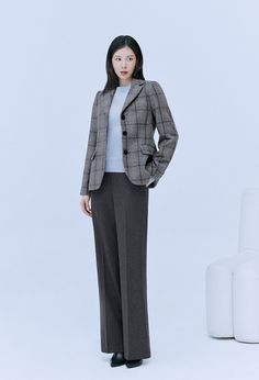 a woman standing in front of a white background wearing a gray suit and black shoes