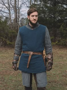 a man dressed in medieval clothing standing in the grass with his hands on his hips