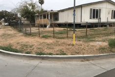 an empty lot in front of a house with a fence around it and a street sign on the corner