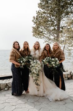 four bridesmaids pose for a photo in front of the water with their bouquets