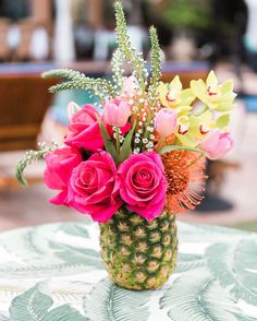 a pineapple vase filled with pink flowers on top of a green table cloth next to a pool