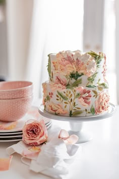 a three layer cake with pink flowers on it and plates around the cake, ready to be cut