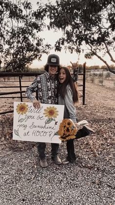 two people standing next to each other in front of a fence holding a sign that says you are my sunshine