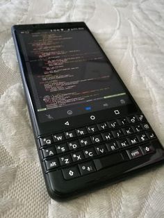 a black blackberry phone sitting on top of a white bed sheet with the keyboard open